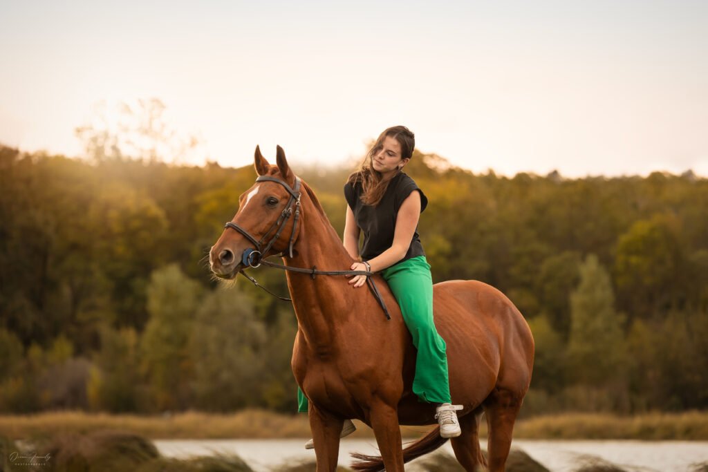 Cheval alezan et sa cavalière à cru devant un couché de soleil sur l'eau Cheval alezan couché de soleil